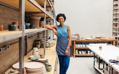 Happy young ceramist smiling at the camera in her pottery - obrazy, fototapety, plakaty