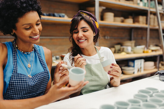 Happy young craftswomen decorating their handmade ceramic cups - Powered by Adobe