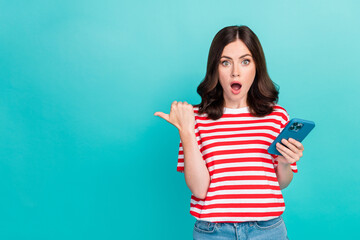 Photo of young attractive funny girlish lady wear red striped t-shirt hold phone shocked finger point empty space follow youtube isolated on cyan color background