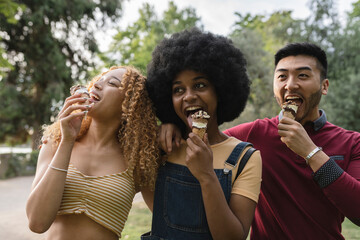 A group of diverse young adults are in the park in a group eating ice cream together. happy...