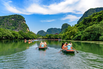 Tourists sitting on rowing boats enjoy the beautiful scenery of rivers and mountains in Trang An, Ninh Binh province, Vietnam.