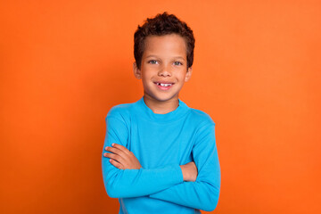 Photo of positive attractive boy arm folded dressed blue stylish sweater clothes good mood isolated on orange color background