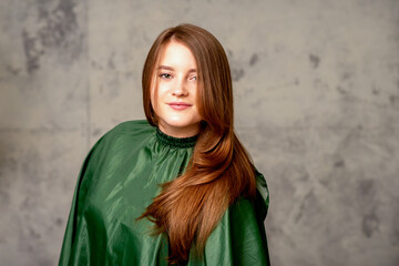 The fashionable young woman. Portrait of the beautiful female model with long hair and makeup. Beauty young caucasian woman with a brown curly hairstyle on the background of a gray wall