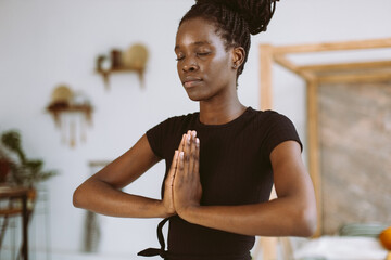 Cropped closeup and meditating young African American woman in black sportswear practicing yoga...