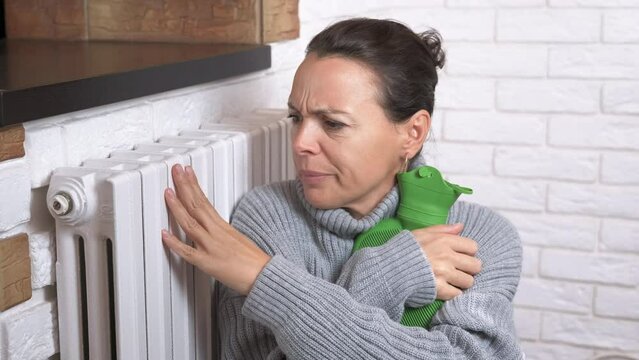 Woman relax with heating pad. A woman try to relax and get warm with heating pad by the radiator. A concept of problems with winter heating period.