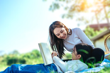 Happy asian family mom and her doughter in the garden, They are having fun and reading book together