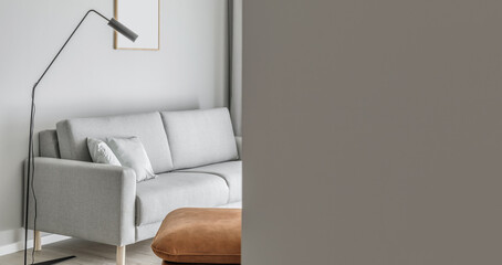 Modern minimalistic living room interior with grey sofa, leather seat, black elegant lamp. Aesthetic simple interior design concept.