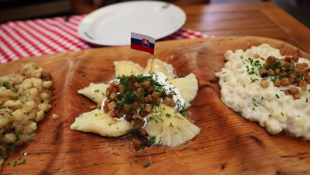 Typical Slovak food served in a cutting board with the national flag, Bryndzov&eacute; halu&scaron;ky and Bryndzov&eacute; pirohy.