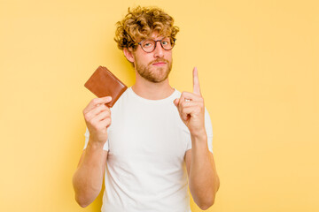 Young caucasian man holding a wallet isolated on yellow background showing number one with finger.