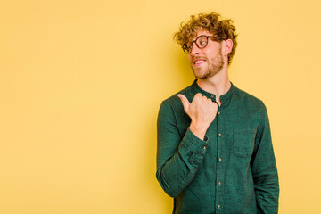 Young caucasian man isolated on yellow background points with thumb finger away, laughing and carefree.