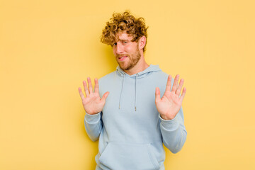 Young caucasian man isolated on yellow background rejecting someone showing a gesture of disgust.