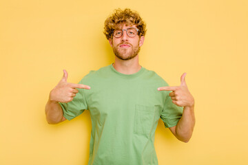 Young caucasian man isolated on yellow background person pointing by hand to a shirt copy space, proud and confident