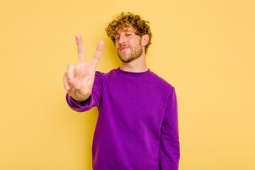 Young caucasian man isolated on yellow background joyful and carefree showing a peace symbol with fingers.