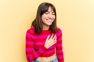 Obraz premium Young caucasian woman isolated on yellow background laughs out loudly keeping hand on chest.