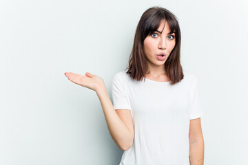 Young caucasian woman isolated on white background impressed holding copy space on palm.