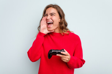 Young caucasian gamer woman holding a game controller isolated on blue background shouting and holding palm near opened mouth.