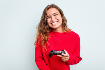 Young caucasian gamer woman holding a game controller isolated on blue background laughing and having fun. © Asier
