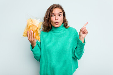 Young caucasian woman holding potato crips isolated on blue background having some great idea, concept of creativity.