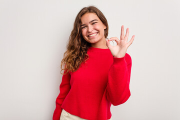 Young caucasian woman isolated on blue background cheerful and confident showing ok gesture.