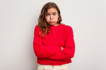 Young caucasian woman isolated on blue background blows cheeks, has tired expression. Facial...