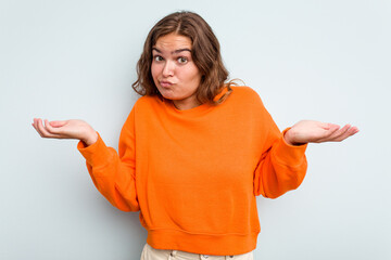 Young caucasian woman isolated on blue background doubting and shrugging shoulders in questioning...