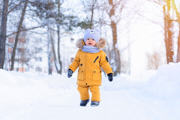 A baby sees snow for the first time. Portrait of a toddler 15-20 months old in yellow warm clothes in a winter park happily looking at snowflakes
