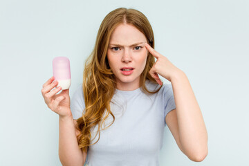 Young caucasian woman holding deodorant isolated on blue background showing a disappointment...