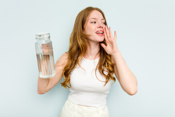 Young caucasian woman holding jar of water isolated on blue background shouting and holding palm near opened mouth.