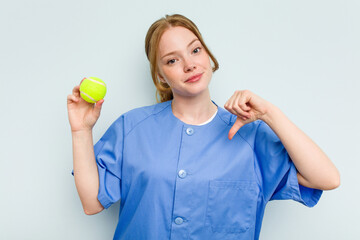 Young caucasian physiotherapist holding a tennis ball isolated on blue background feels proud and self confident, example to follow.