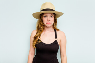 Young caucasian woman going to the beach isolated on blue background shrugs shoulders and open eyes confused.