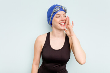 Young caucasian swimmer woman isolated on blue background shouting and holding palm near opened mouth.