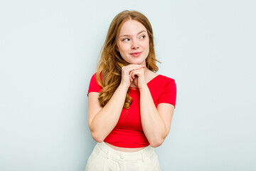 Young caucasian woman isolated on blue background keeps hands under chin, is looking happily aside.