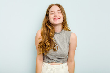 Young caucasian woman isolated on blue background laughs and closes eyes, feels relaxed and happy.