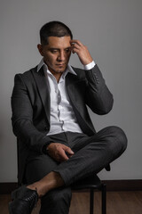 sitting on a chair a worried young latin man with short hair, business clothes, suit and shirt, fashion and lifestyle in studio