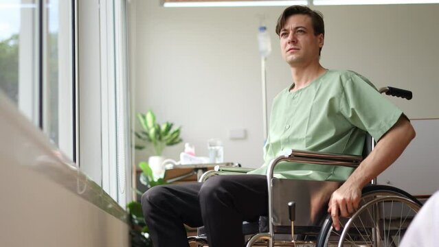 Young man patien sit in the  wheelchair while turn direction to the windows.