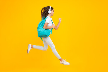 Fototapeta na wymiar School girl, teenager student in headphones on yellow isolated studio background. Music school concept. Excited teenager, school leisure. Jump and run, jumping child.