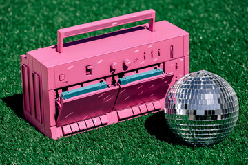 Retro tape recorder and disco ball on green grass