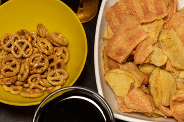 Close-up of a table with a small bowl of pretzels, a plate of chips, a soda, and a beer