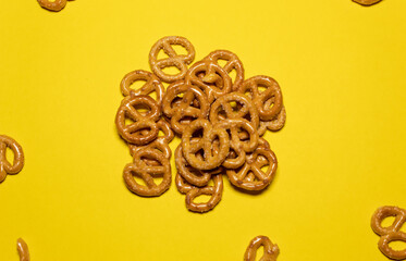 A group of small pretzels together and others scattered around on a yellow background