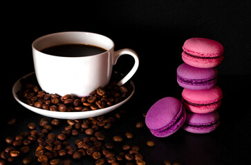 A white cup of coffee stands on the table next to the coffee beans on a black background.