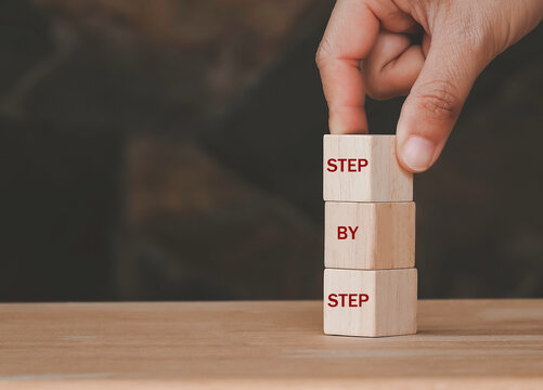 Hand arranging wood block stacking as step stair on top with word Step By Step. Business concept for personal ladder of success process.