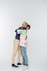 side view of young and stylish gay and queer person embracing on grey background.