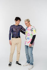 young and happy gay and nonbinary person hugging on grey background.