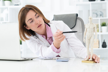 Young attractive female doctor sitting at the desktop in the office and consulting her patient online