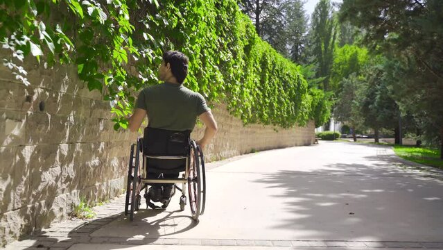 Young Man With Paralyzed Legs In A Wheelchair Walks Alone Through The City Streets.
Disabled young man gets into wheelchair on the street in summer day. Manually moving and turning the wheels.
