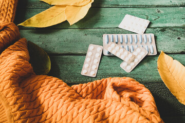 Many blister of pills on background with yellow fall leaves and warm sweater, seasonal flu concept