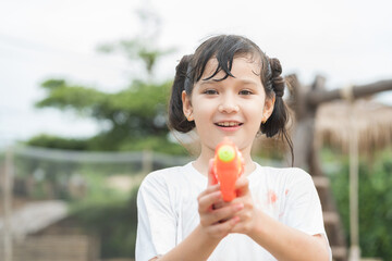 Child girl has fun playing with water gun on hot summer day outdoors. Kid girl having fun with water outdoors