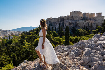 Rear view of tourist woman wearing a white dress and golden laurel crown looking at Parthenon of...