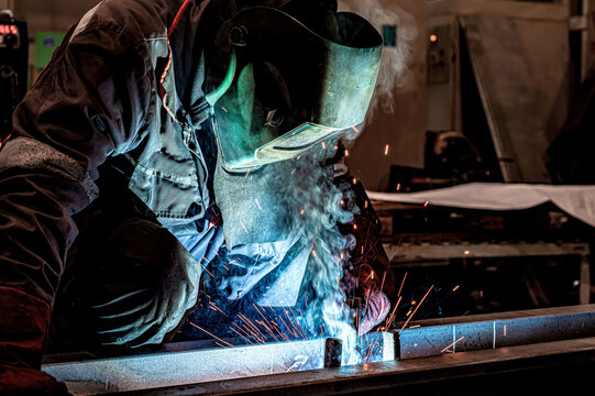 A welder welds long beams with a gas welding machine at an industrial plant.