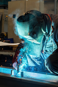 A welder welds long beams with a gas welding machine at an industrial plant.